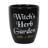 A black ceramic plant pot with the text 'WITCH'S HERB GARDEN' written in white and gold letters, along with a decorative leafy design.